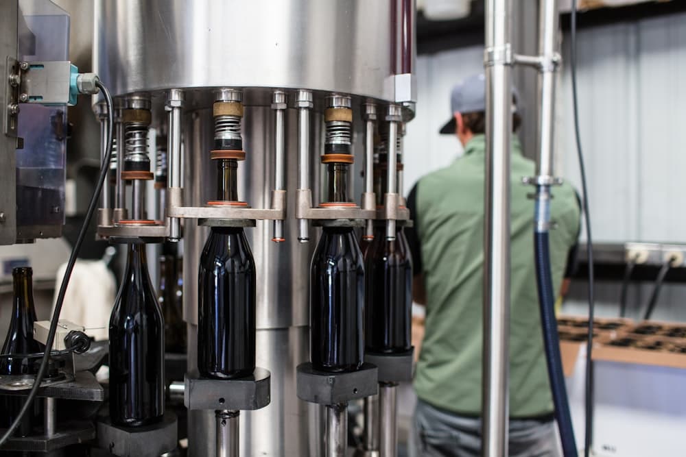 Capped bottles massed on the outfeed of a bottling plant, and unlabelled bottles under a rotary filler