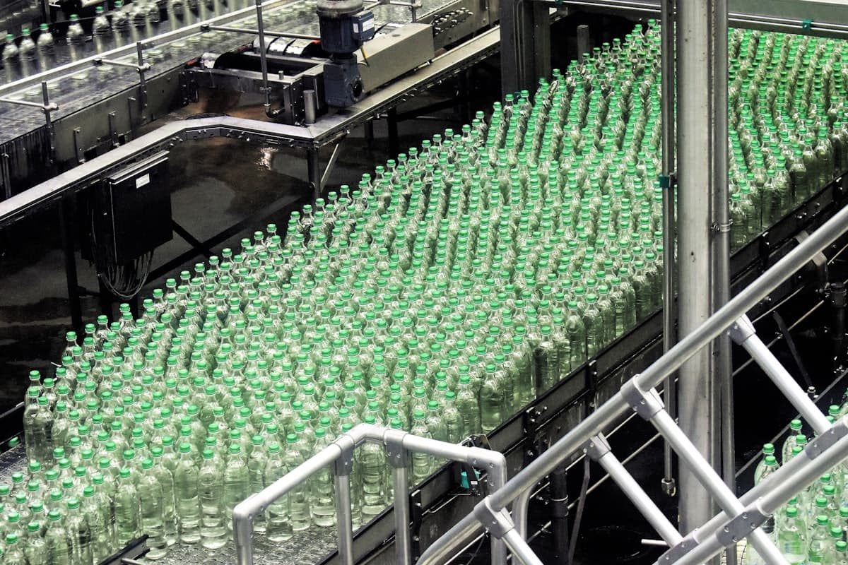 Capped bottles massed on the outfeed of a bottling plant, and unlabelled bottles under a rotary filler
