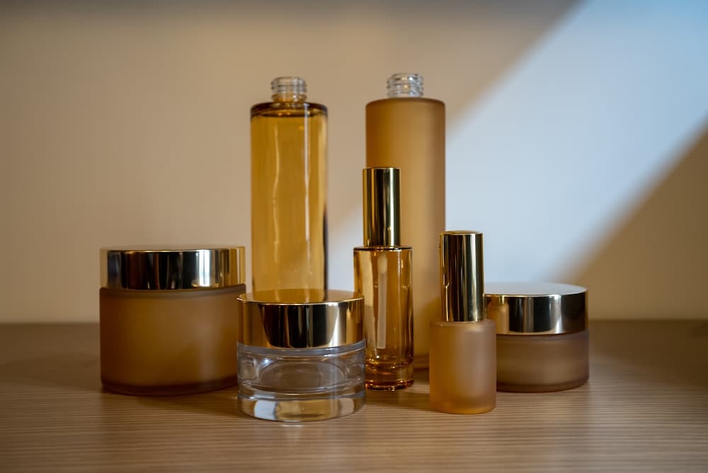 Unlabelled amber glass jars and bottles, and a filling head dosing white bottles on a conveyor